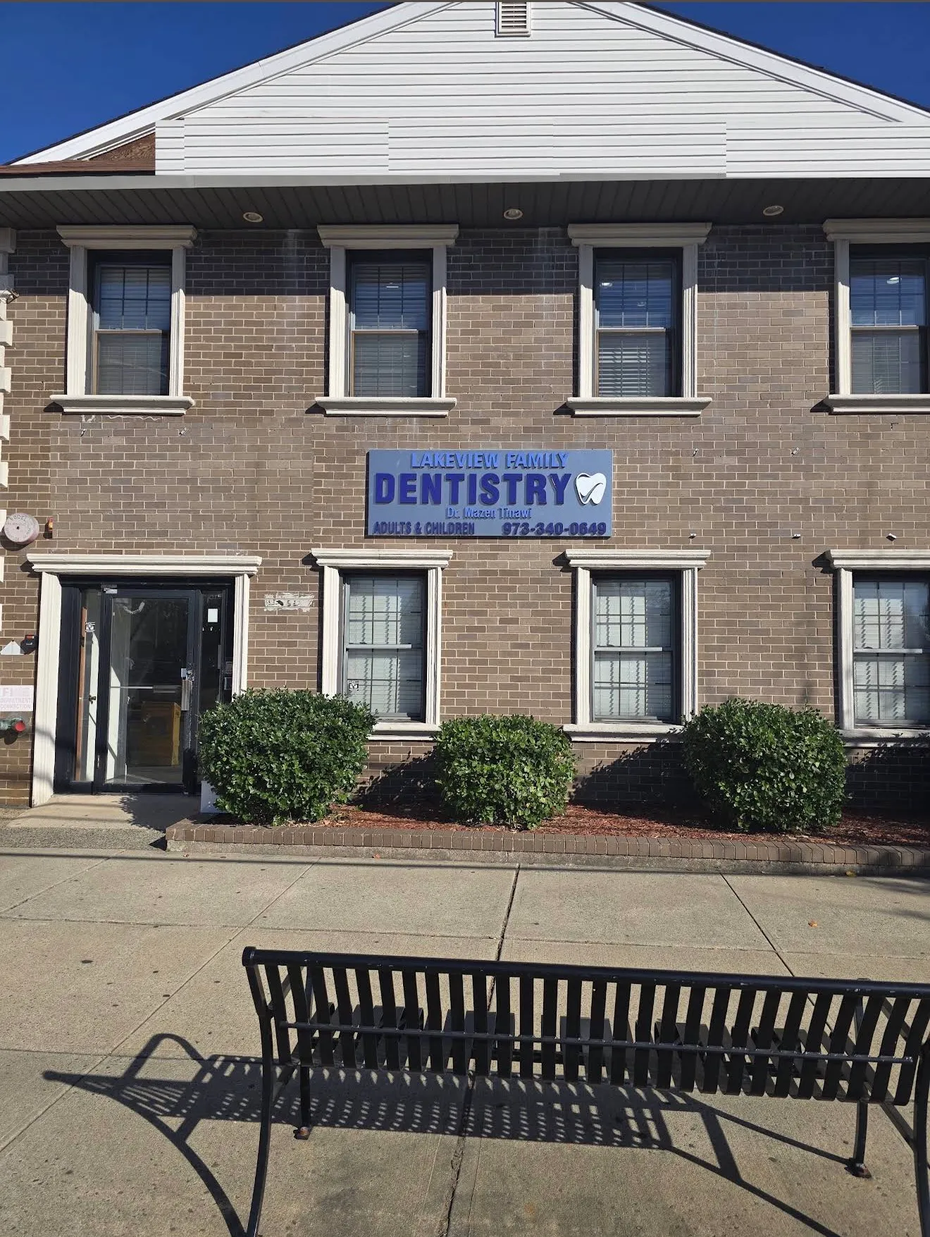 The front of the Lakeview Family Dentistry building from the sidewalk, a brick facade with the blue practice sign and a bench out front.