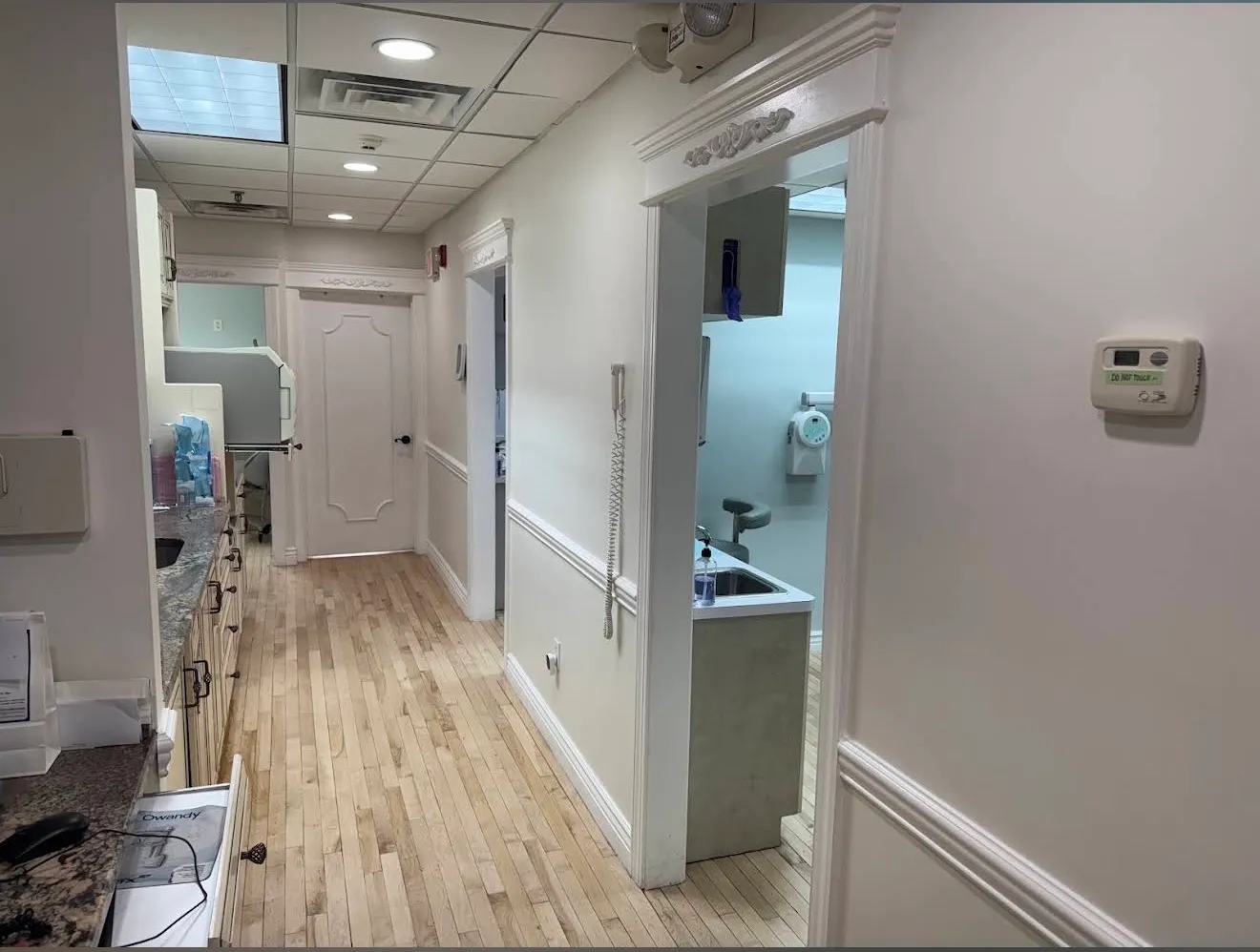 A bright treatment-room corridor with wainscoted walls, wood floors and a restroom off to the side.