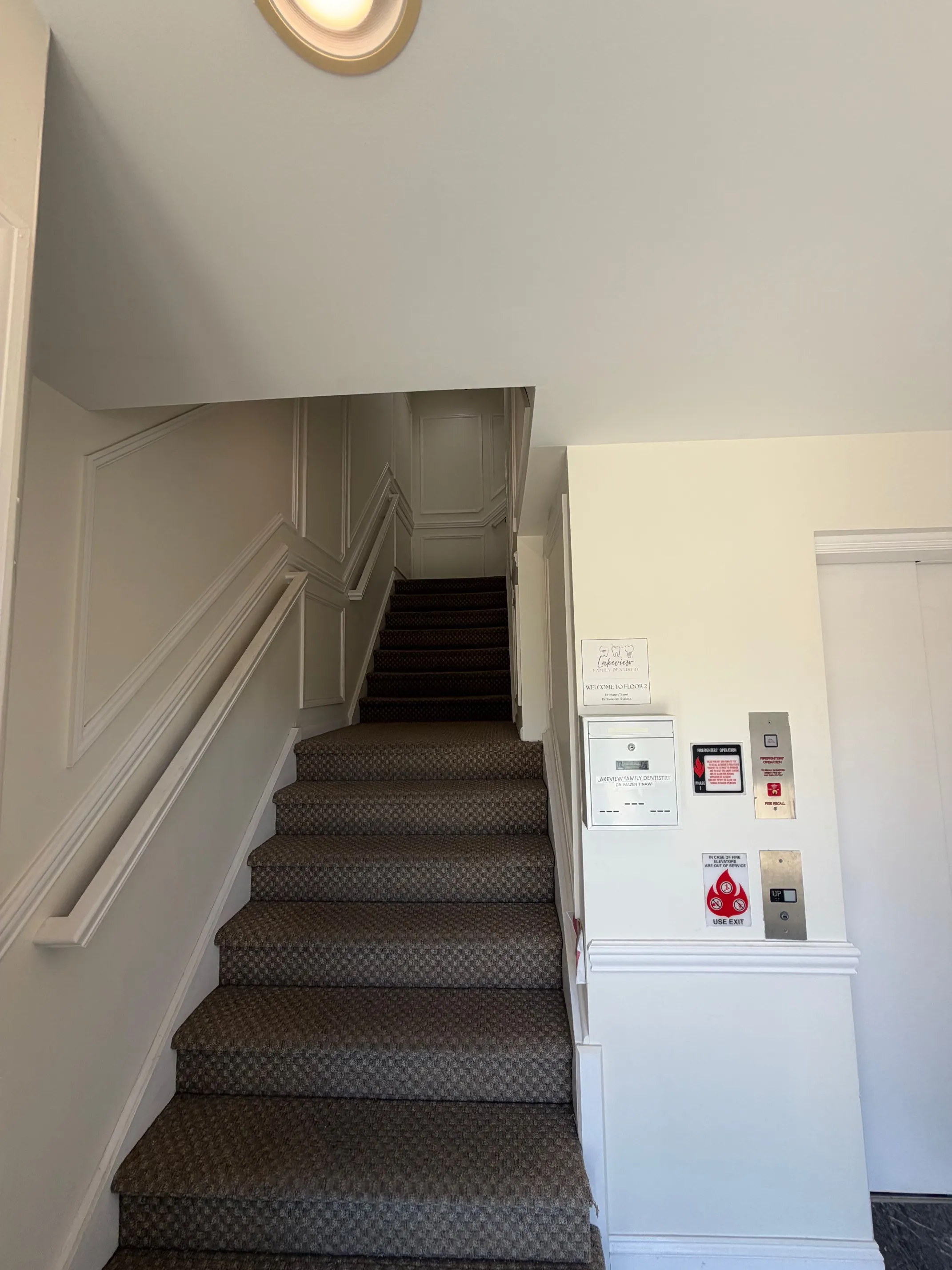 The ground-floor entrance, with carpeted stairs up to the office and the elevator call button beside a Lakeview Family Dentistry welcome sign.