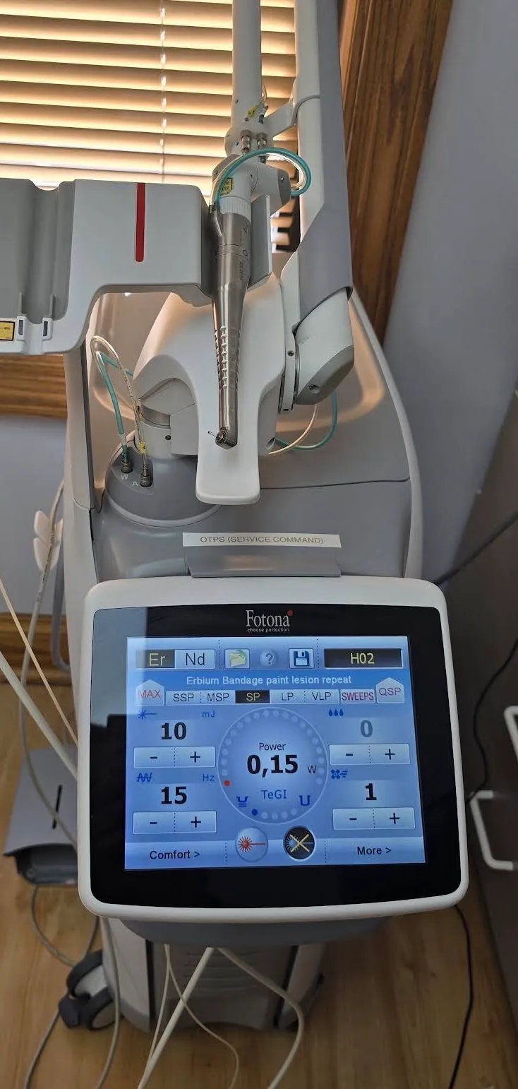 A Fotona dental laser on a rolling stand, its handpiece stowed on the arm above and its touchscreen showing the settings for a treatment.