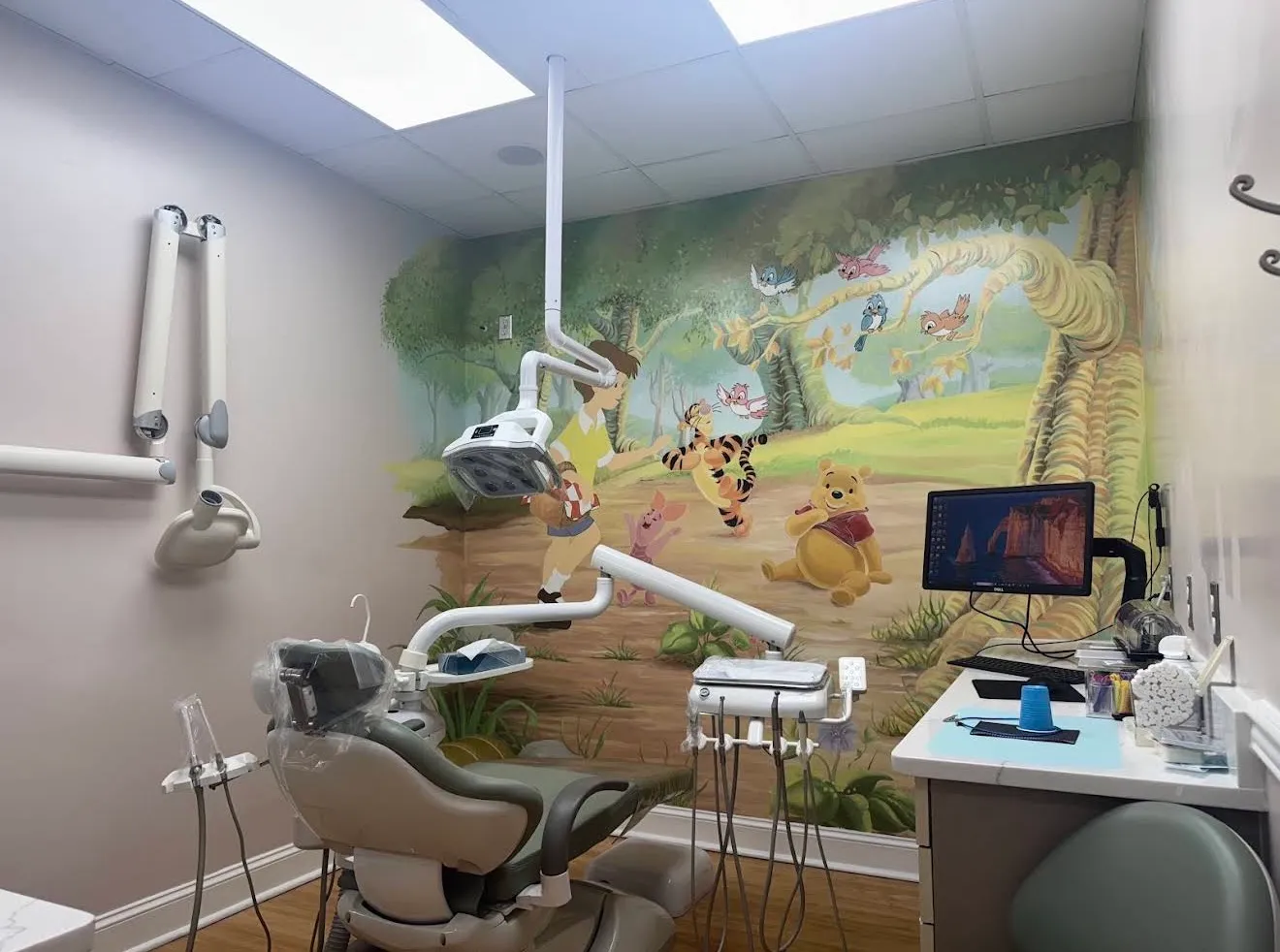 The children's treatment room, one wall painted with a Winnie the Pooh woodland mural, the chair and monitor alongside it.
