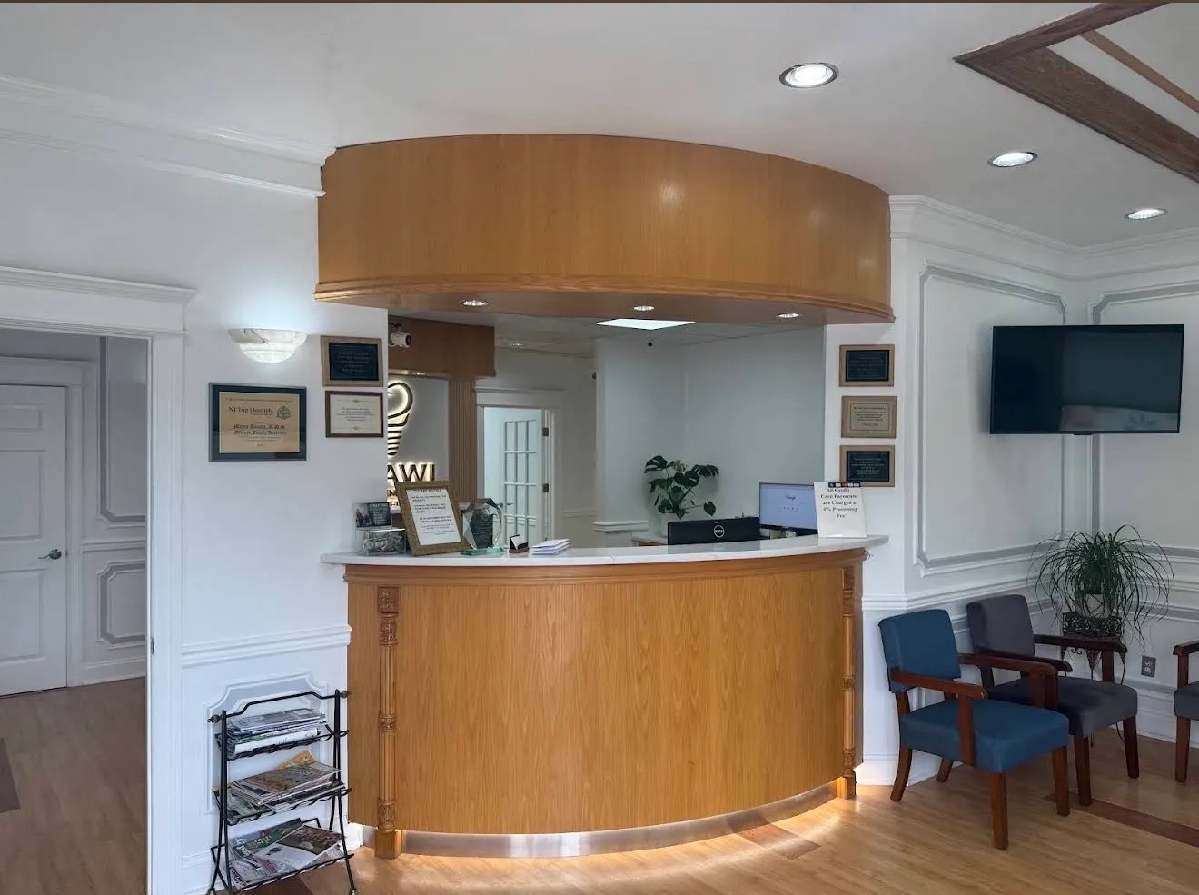 The front desk: a curved oak reception counter beneath a matching rounded soffit, framed certificates on the wall to either side, and armchairs in the waiting area beyond.