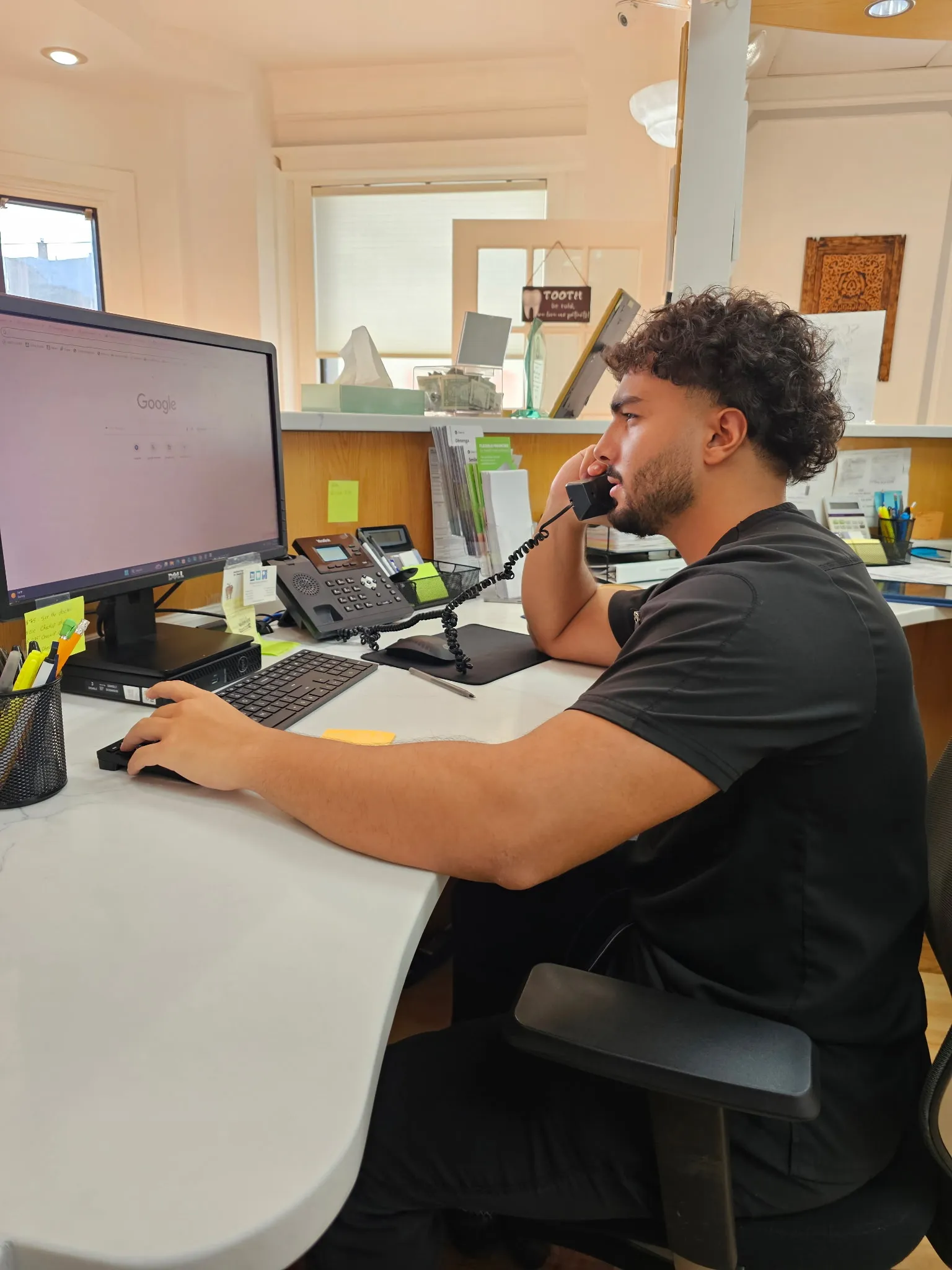 A team member at the front desk taking a call, with the reception counter and patient information leaflets behind.
