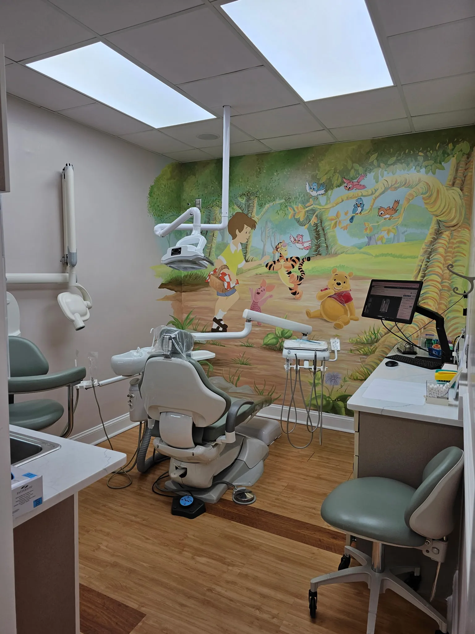 The children's treatment room, with a hand-painted storybook woodland mural behind a mint-green dental chair.