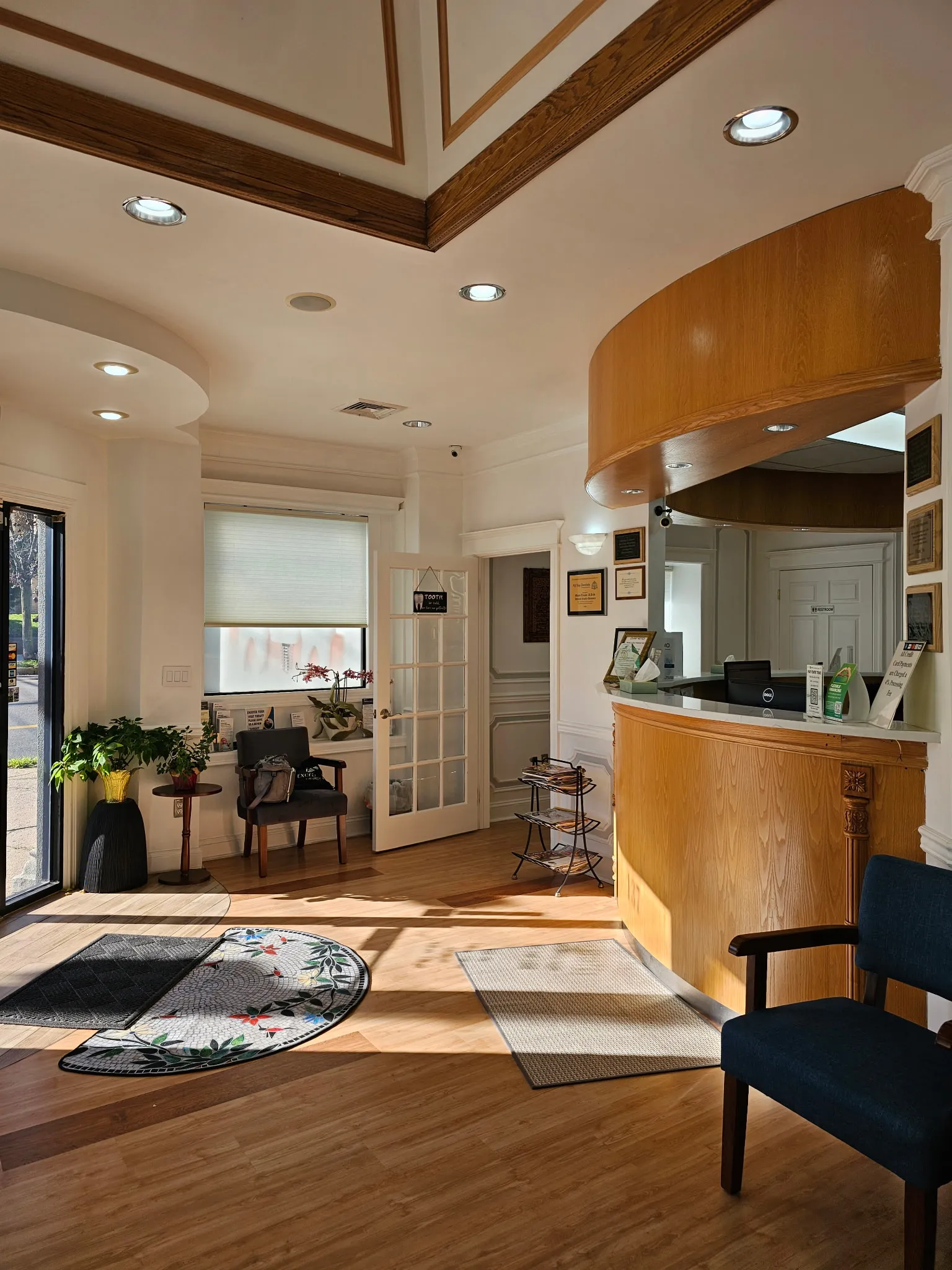 The entrance and reception area, with a curved oak front desk, plants by the window and a mosaic rug inside the door.